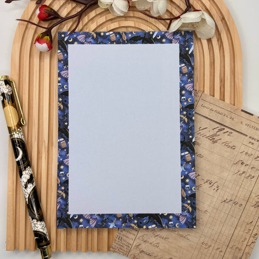 Notitieblok met fantasy border van draken, boeken, sterren, manen en zwaarden – Draconic Dreams design.